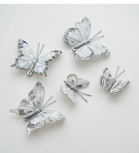 Dettaglio di cinque fermagli a farfalla bianchi con glitter argento e perle finte