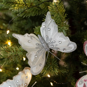 Elegante farfalla di Natale bianca con paillettes appesa a un ramo di pino illuminato