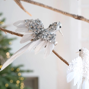 Uccellini natalizi con paillettes argento e piume bianche su ramo di un albero