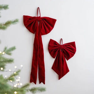 Set of large burgundy velvet Christmas bows hanging on wall with festive tree background