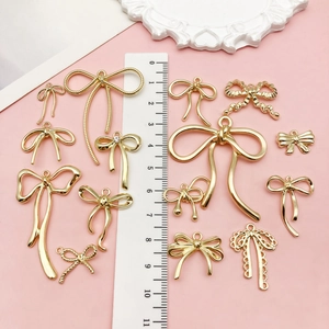 Surtido de colgantes de lazo dorado para joyería DIY sobre fondo rosa con regla