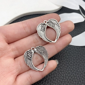 Close-up of retro silver angel wing pendants with heart-shaped hollow design held by hand