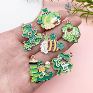 Détail macro de pendentifs trèfle en émail vert tenus en main pour l'échelle