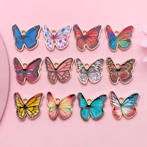 Flat lay of colorful butterfly charms for DIY jewelry on a soft pink background