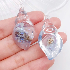 Gros plan d'un pendentif coquillage translucide avec sable, paillettes et coquillages