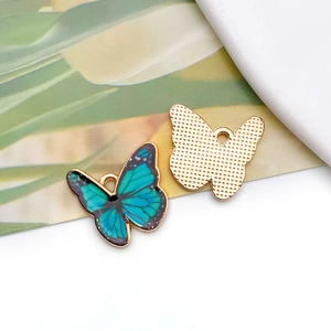 Macro detail of butterfly charm showing blue-green enamel front and textured gold back