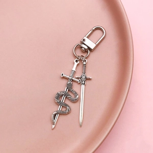 Antique silver sword and snake pendant keychain on a pink ceramic dish display