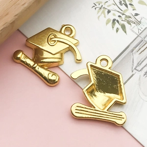 Detailed close-up of golden alloy graduation cap and scroll charms for DIY jewelry making