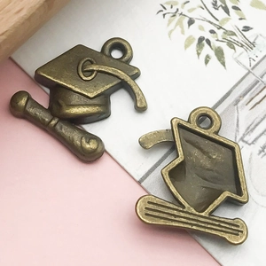 Macro view of bronze alloy graduation cap and scroll charms for DIY jewelry making