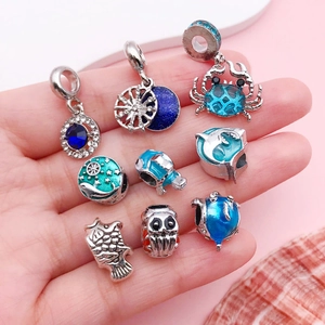 Mano con ciondoli marini come granchi e perle smaltate blu per braccialetti fai-da-te