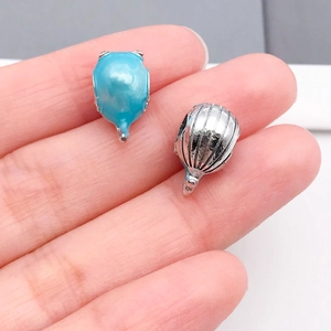 Dettaglio di ciondoli marini in smalto blu e argento tra le dita per la dimensione