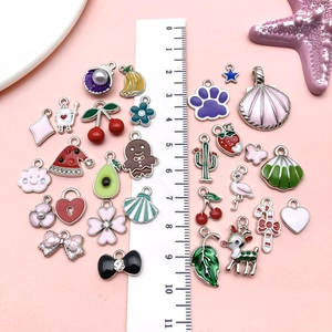 Flat lay of colorful DIY enamel charms including fruits and animals on pink background