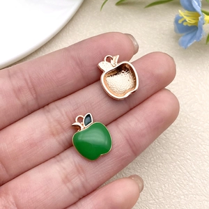 Detail of green enamel apple pendant charm for DIY jewelry being held for size