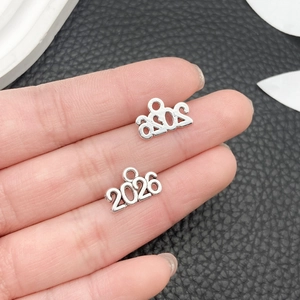 Primer plano de dijes plateados con el año 2026 para joyería DIY en la mano