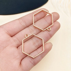 Close-up of hexagonal gold-plated DIY jewelry frames held in hand for size scale