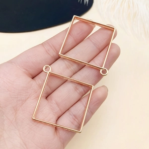 Close-up of hand holding two square gold plated hollow frames for DIY jewelry making