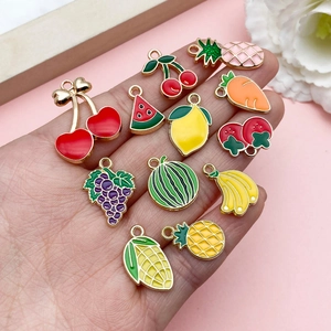 Variety of colorful enamel fruit and vegetable charms held by hand for DIY jewelry making