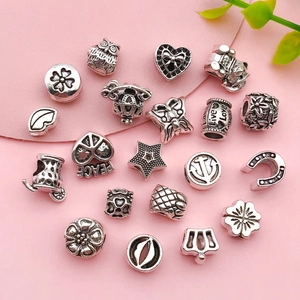 Varietà di perline vintage in argento con motivi a cuore e stella su fondo in pelle rosa