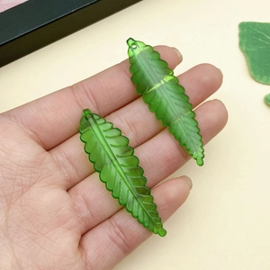 Primer plano de colgantes de hoja de arce en acrílico verde con agujeros para artesanía DIY