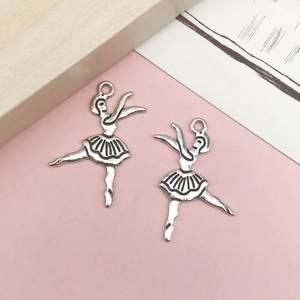 Detalle de dijes de bailarina en plata antigua para joyería DIY sobre fondo rosa suave