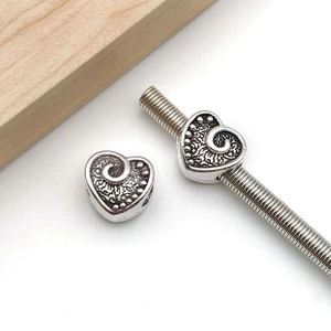 Dettaglio di perline distanziatrici a forma di cuore argento con motivi a volute per gioielli