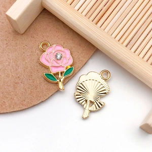 Close-up of pink enamel rose flower charm with sparkling rhinestone and green leaf detail