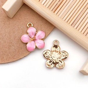 Detail of pink enamel flower charms and golden alloy pendants for DIY jewelry crafts