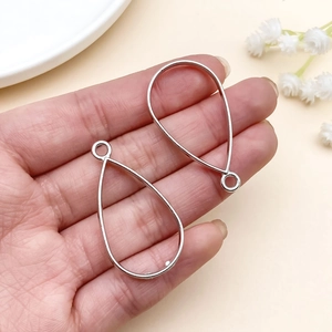 Handheld view showing silver teardrop metal frames for DIY jewelry with small rings