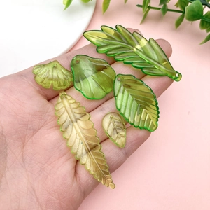Hand mit verschiedenen grünen Acryl-Blattanhängern für DIY-Schmuck und Dekorationen