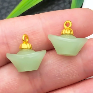 Macro view of two mini gold-capped faux jade pendants in traditional ingot shape