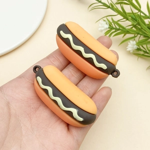 Detailed view of handmade miniature hot dog resin pendants held in hand for scale