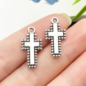 Vue détaillée de pendentifs croix en argent vintage avec bordure perlée sur les doigts