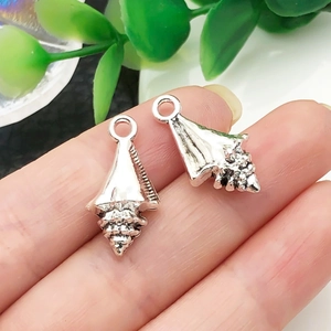 Macro shot of silver conch shell charms in hand showing detailed spiral ocean textures