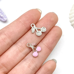 Detail shot of cherry-shaped jewelry charms in silver and pink enamel with jump rings