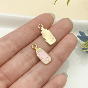 Detalle de colgantes de biberón en esmalte rosa con chapado de oro y grabado de rayos de sol