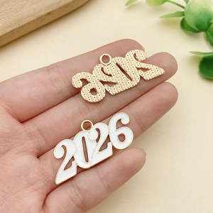 Detalle macro de colgantes año 2026 en oro y esmalte blanco para joyería DIY
