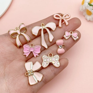Pink enamel bow charms collection for DIY jewelry making displayed in hand