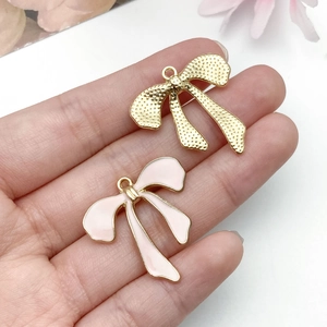Detail of pink oil drip and gold alloy bow pendants for DIY jewelry and accessories