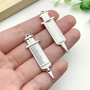 Detailed syringe-shaped metal charms with white enamel and silver texture in hand
