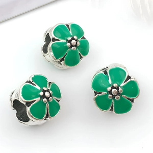 Vista macro de tres dijes de flores de esmalte verde con núcleo plateado para pulseras DIY