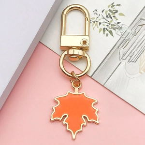Detail of maple leaf keychain with golden metal clasp and orange enamel finish