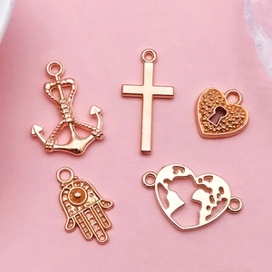 Close-up of five rose gold DIY charms including Hamsa hand, anchor, and heart designs