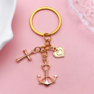 Nahaufnahme des goldenen Schlüsselanhängers mit Kreuz, Anker und Herz auf rosa Grund
