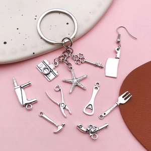 Antik-silberne Werkzeug-Anhänger Set mit Hammer Zange und Kamera auf rosa Hintergrund