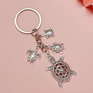 Détail d'un porte-clés tortue argenté avec quatre pendentifs sur fond rose doux