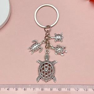 Détails du porte-clés tortue avec dimensions et pendentifs argentés sur un fond rose doux