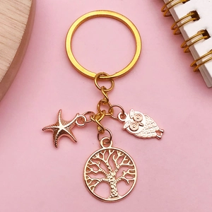 Macro view of KC gold alloy key ring with starfish, tree of life, and owl pendants