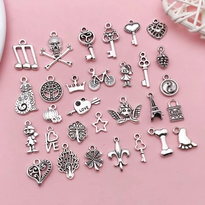 Detailed flat lay of diverse vintage silver alloy pendants for DIY jewelry on pink background