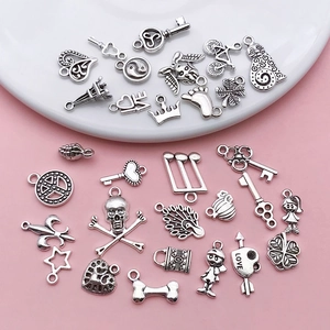 Assorted vintage silver alloy charms for DIY jewelry making in various shapes on a pink surface