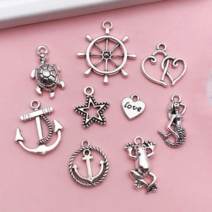 Detailed flat lay of antique silver sea-themed DIY pendants on a pink surface